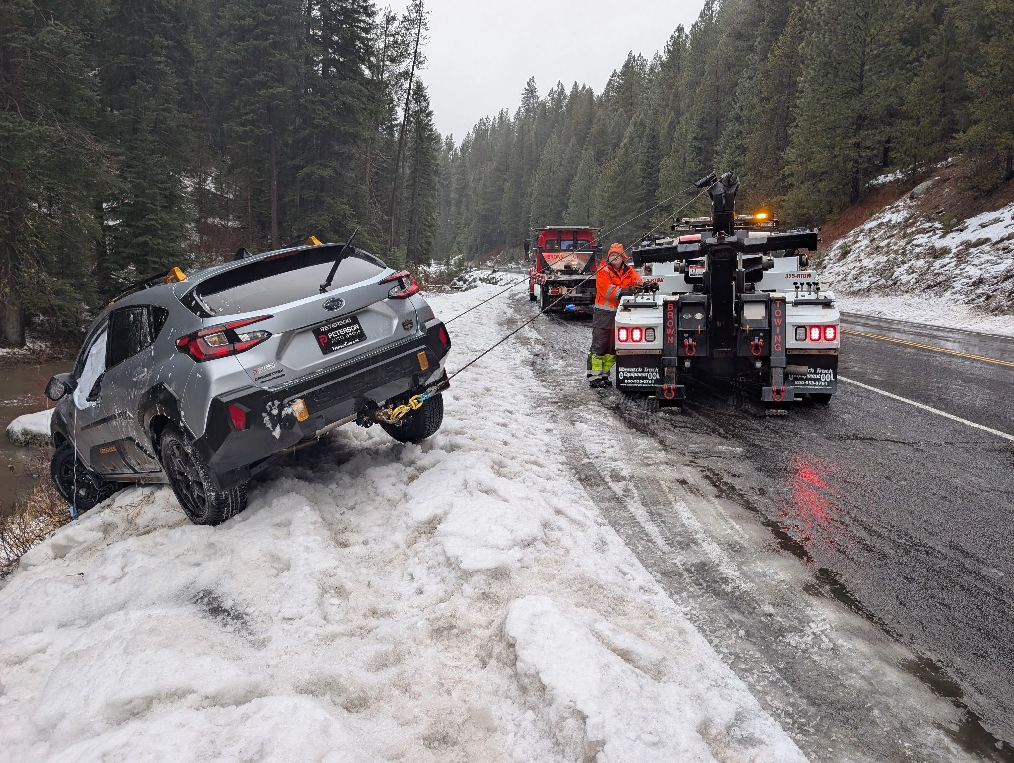 Brown Towing crew winching a Subaru out of a snowy ditch with two recovery trucks